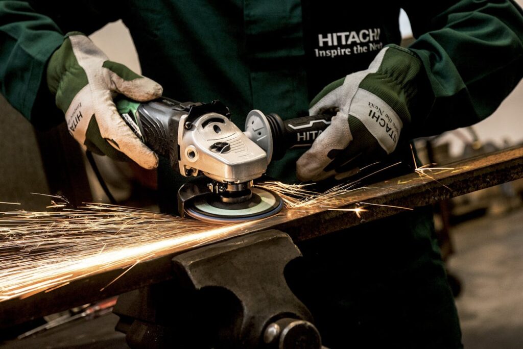grinder-hitachi-power-tool-flexible-162625 A skilled worker using an angle grinder on metal, producing sparks in an industrial workshop.